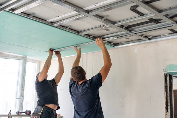 Deux artisans sont en train d'isoler phoniquement plafond en posant des panneaux isolants bleu ciel.