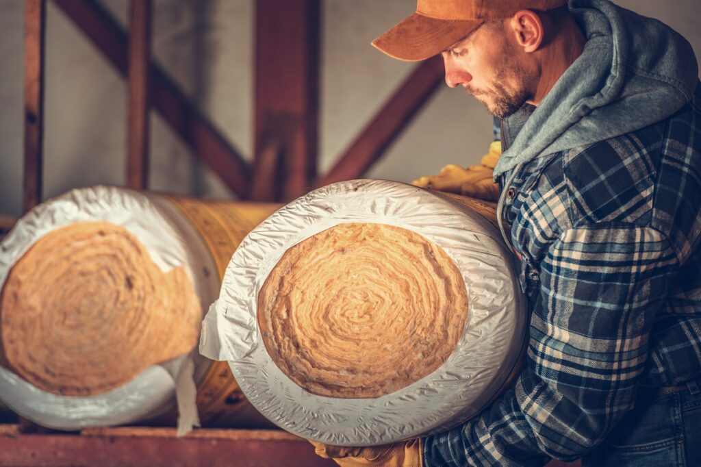 Artisan portant deux rouleaux d'isolant biosourcé.